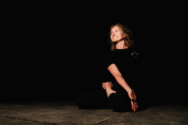 Eine Frau zeigt eine Yoga Stellung vor dunklem Hintergrund.