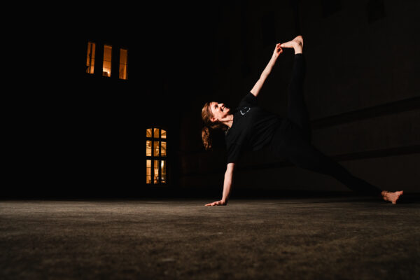 Eine Frau zeigt eine Yoga Stellung vor dunklem Hintergrund.