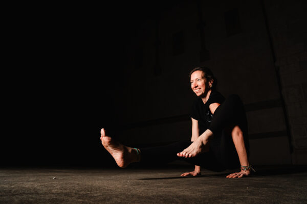 Eine Frau zeigt eine Yoga Stellung vor dunklem Hintergrund.